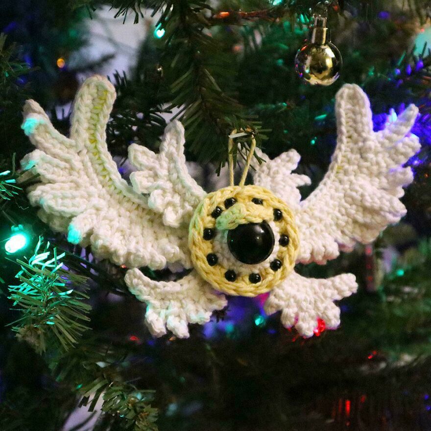 A white crochet creation ornament with wings hangs on a Christmas tree. Crochet craft projects.