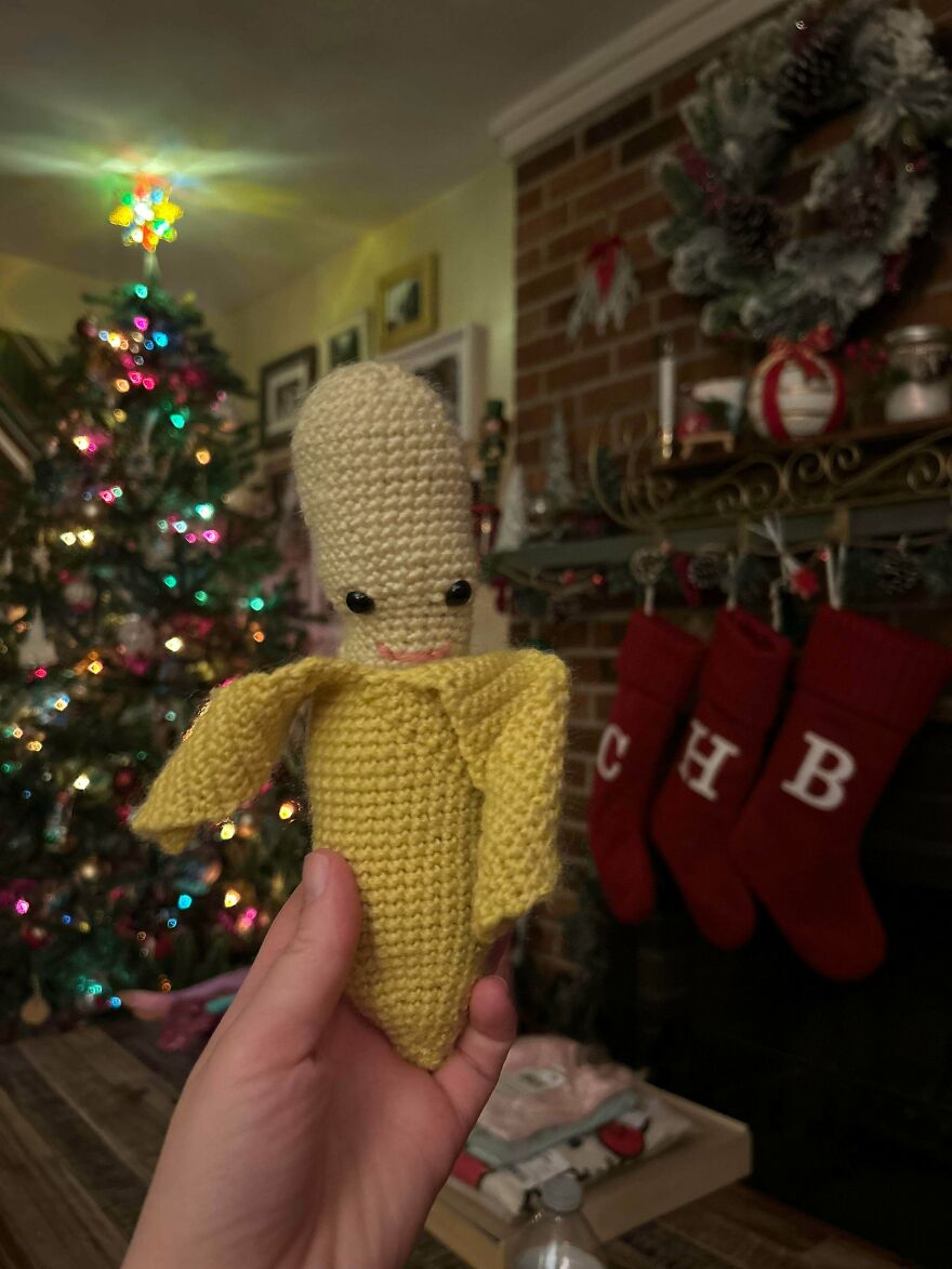 A hand holding a quirky crochet creation of a banana figure in a festive, living room setting.