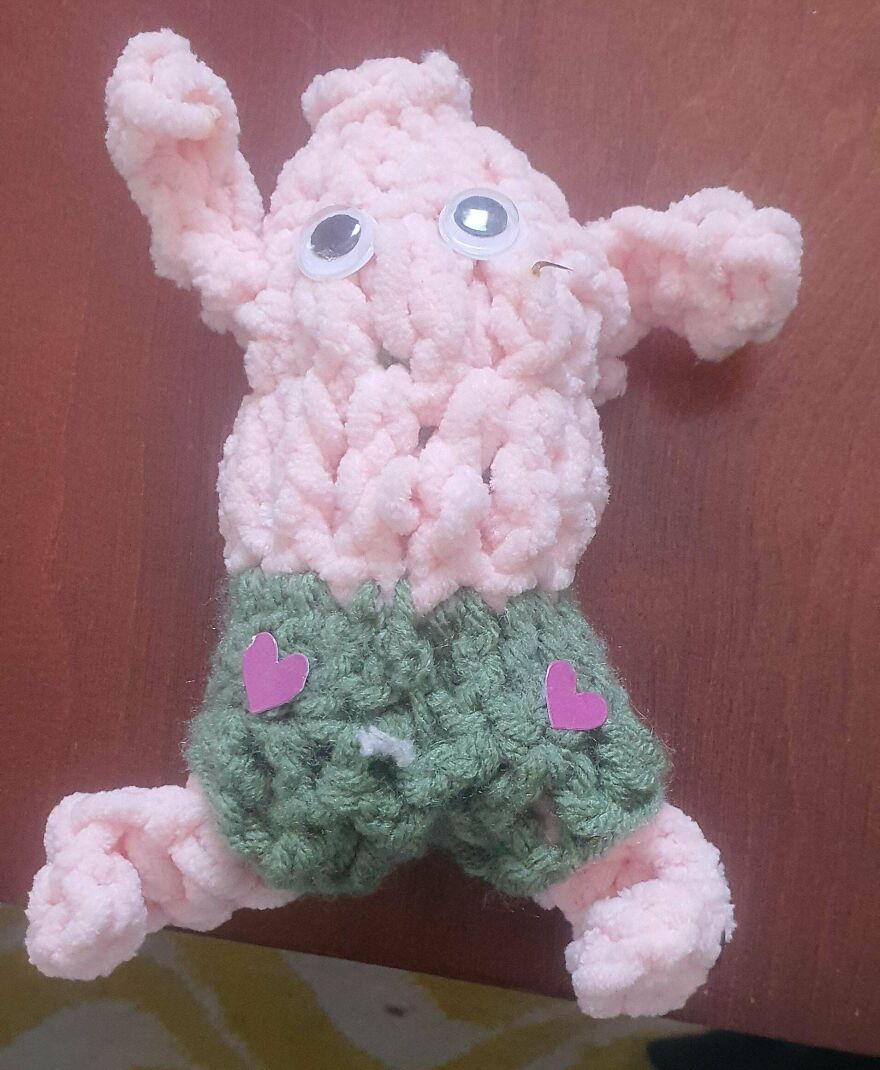 A fluffy pink crochet creation with googly eyes and green shorts featuring pink hearts.