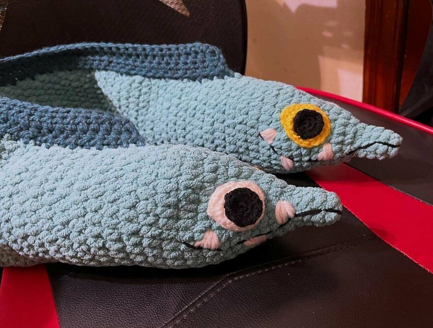 Two charming crochet creations resembling blue-green fish with distinct eyes, resting on a chair.