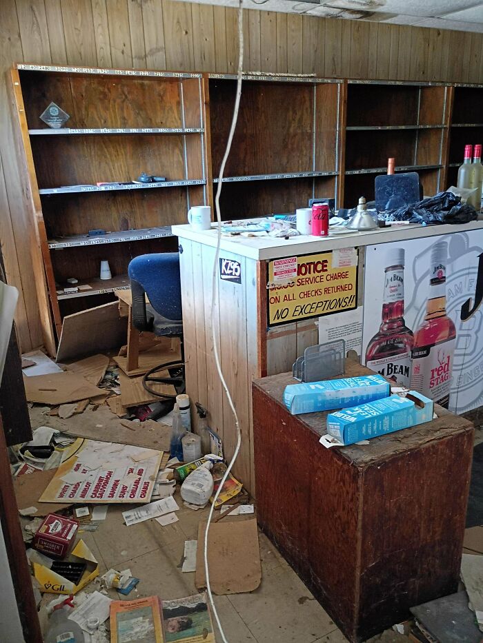A messy, abandoned room with a cluttered counter, empty shelves, and various discarded items on the floor, found while exploring abandoned places.