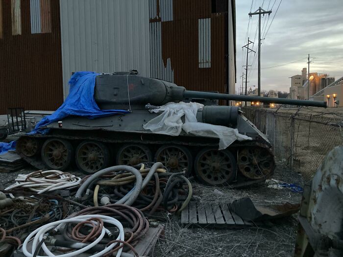 An abandoned military tank covered with tarps, rusting next to a pile of hoses, exploring abandoned places.