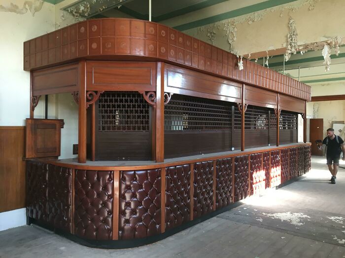 A grand, ornate wooden counter with leather upholstery in a decaying, abandoned building, exploring abandoned places.