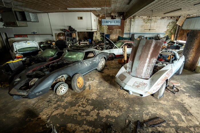 Exploring abandoned places reveals several classic cars needing restoration in a cluttered, dusty garage.