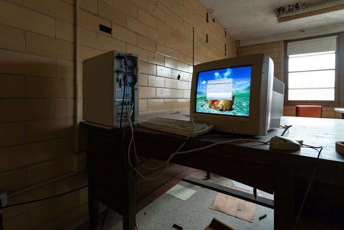 Exploring abandoned places reveals an old computer setup, monitor on a wooden desk in a desolate room.