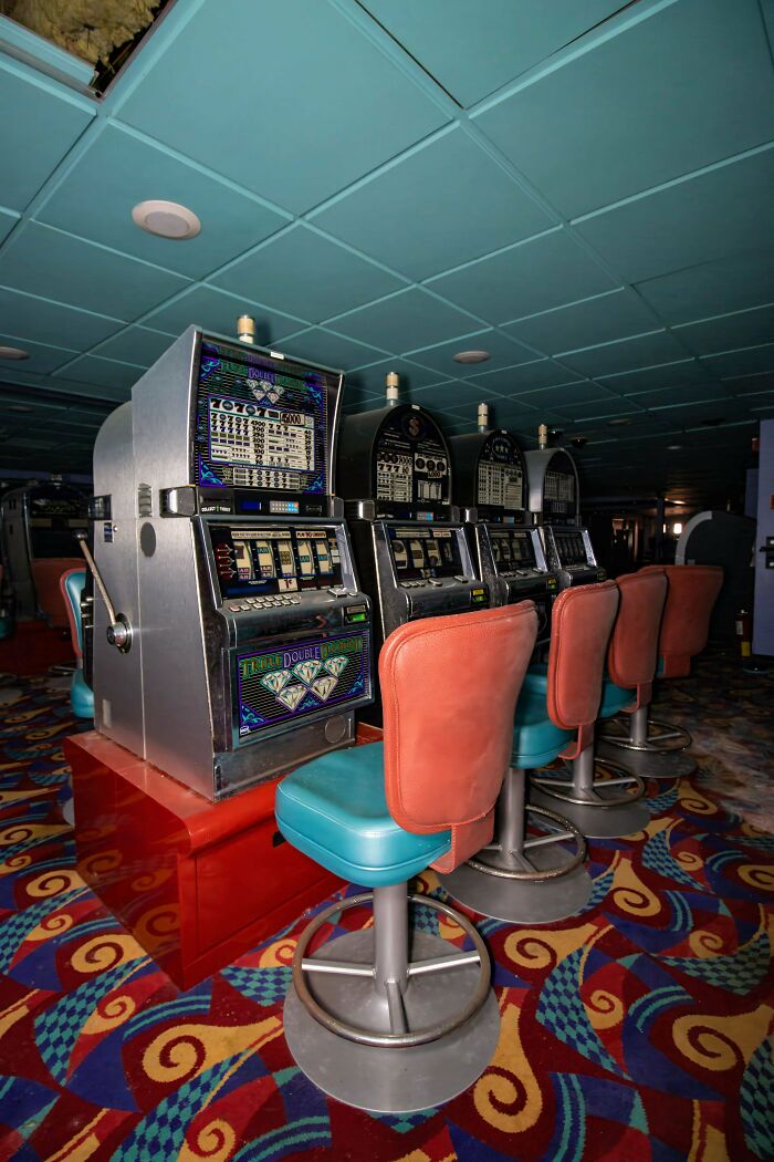 Exploring abandoned places reveals a row of vintage slot machines and stools with a colorful carpet.