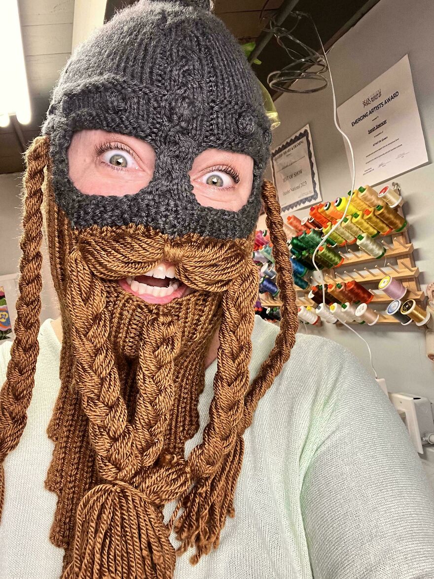 A woman wearing a crochet Viking helmet with braided beard and mustache, a funny craft project.