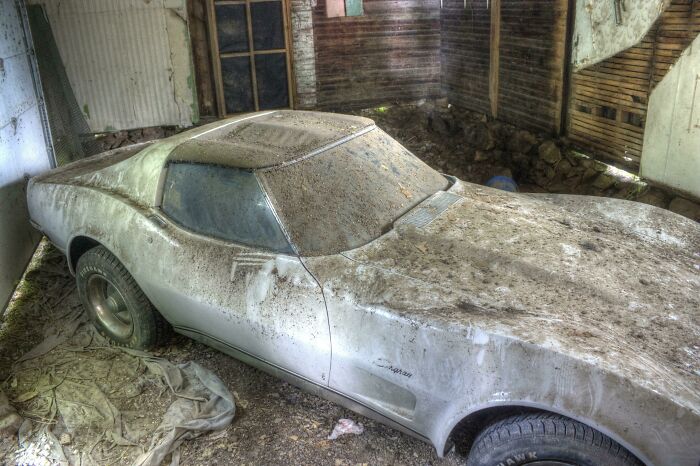 Exploring abandoned places reveals a dust-covered classic car, possibly a Corvette, stored in a rundown garage.