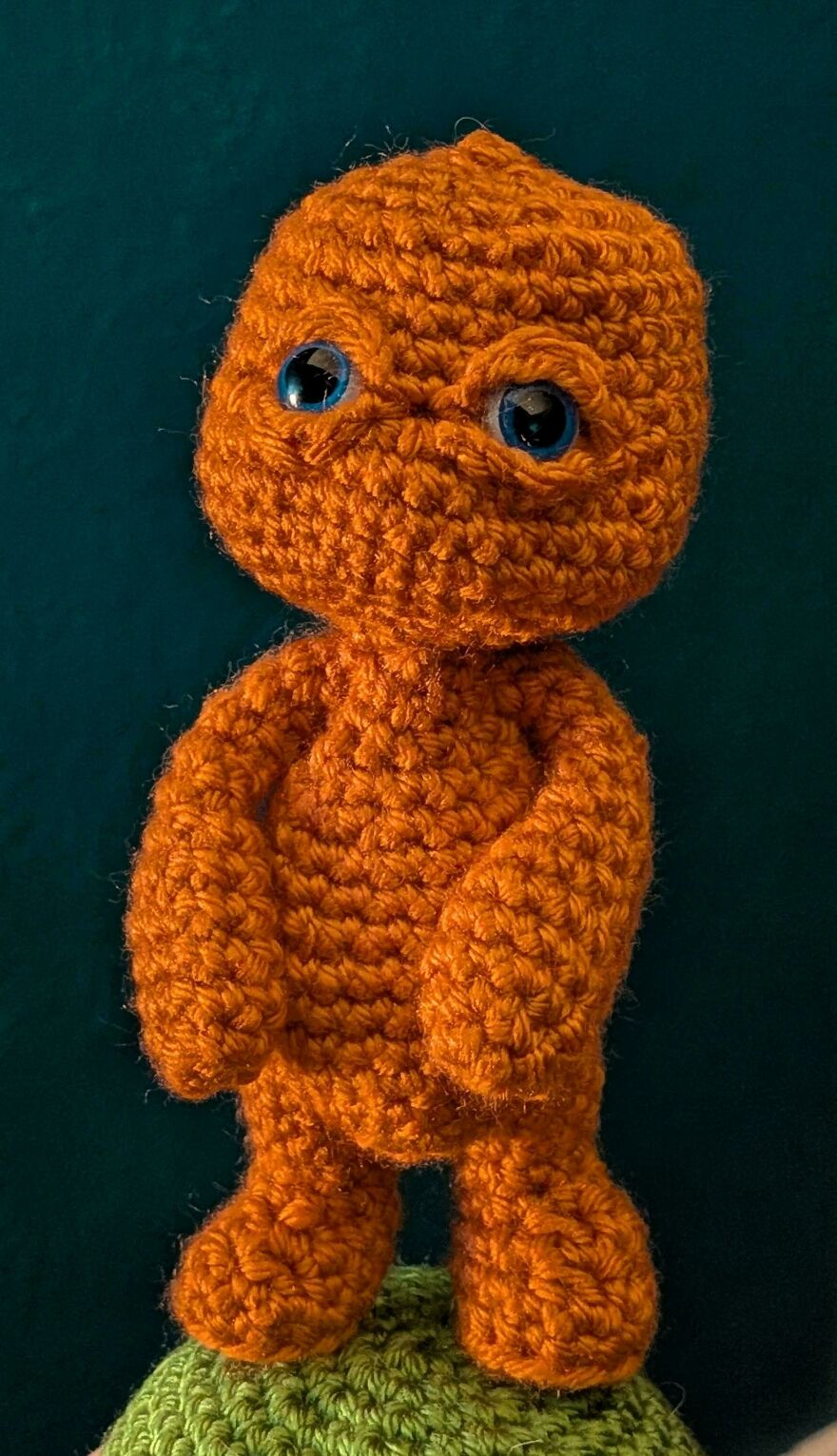 An orange crochet creation doll with blue eyes, standing, showing detailed craft project texture.