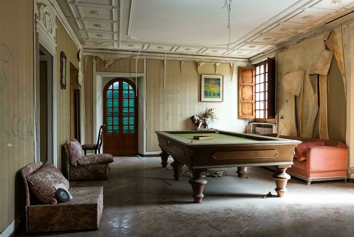 A dusty billiards room with peeling wallpaper and an old pool table, found while exploring abandoned places.