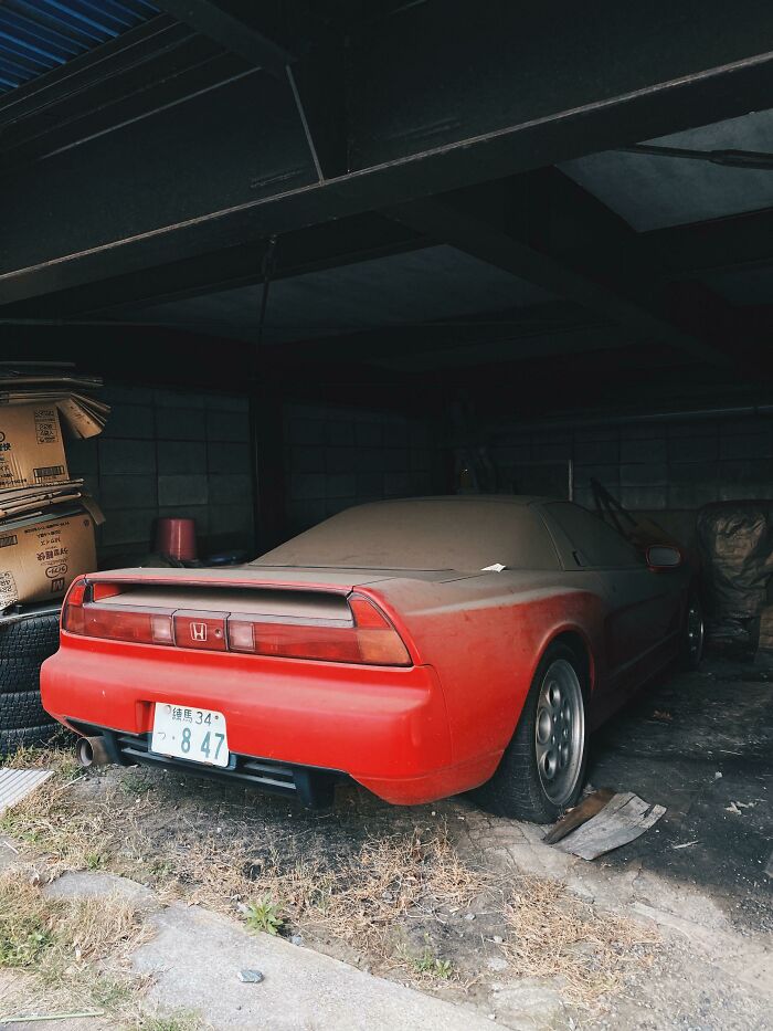 A dusty red sports car parked in a garage, exploring abandoned places and finding something unexpected.