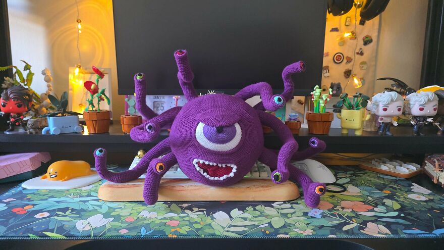 A handmade purple crochet creation of a monster with multiple eyes, displayed on a desk.