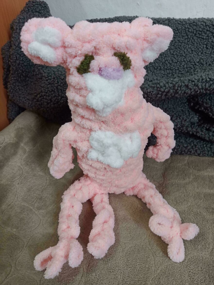 A fluffy pink crochet creation stuffed animal with white accents, resting on a blanket.