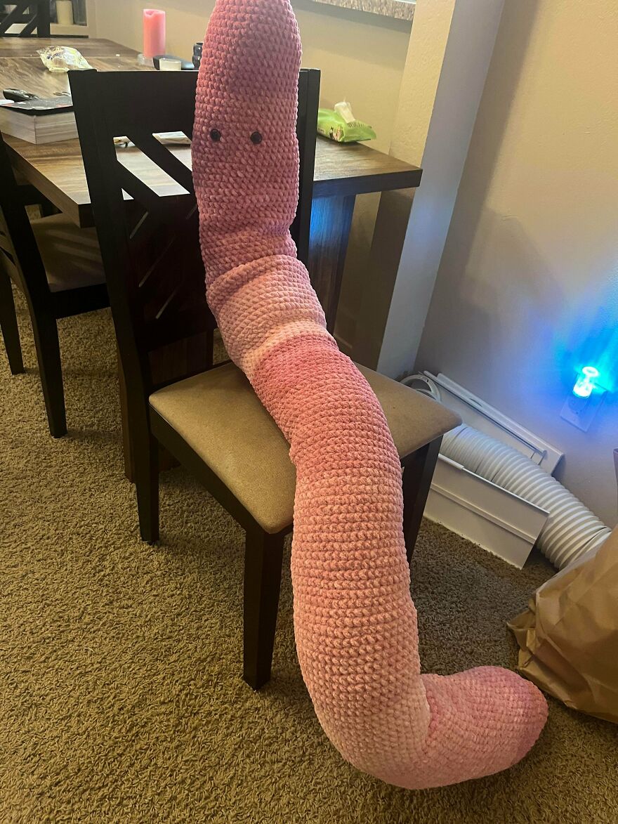 A long, pink crochet creation worm plush toy draped over a dining chair.