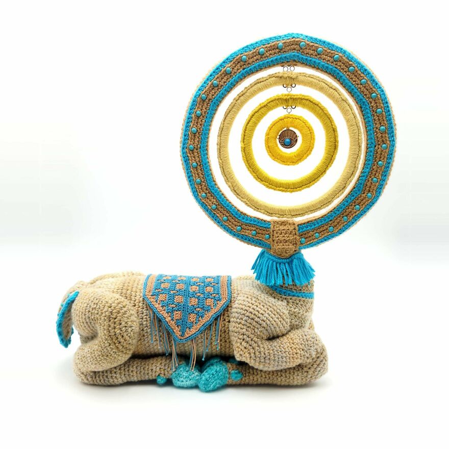 An elaborate crochet creation of a camel with a large, circular, beaded design on its back.