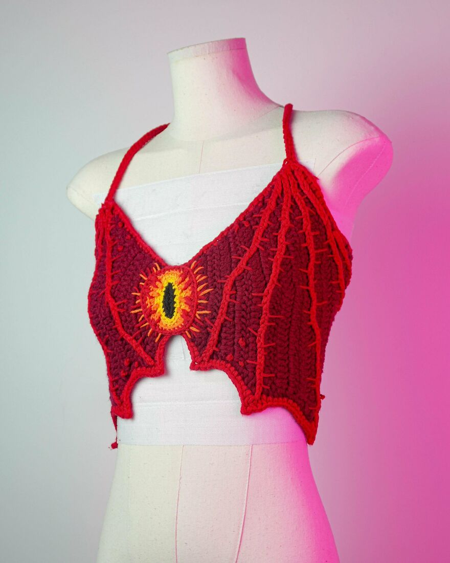 A red crochet crop top on a mannequin, featuring a dragon eye design, demonstrating an intricate crochet creation.