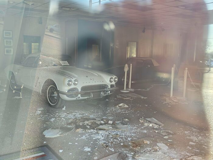 A classic white convertible in an abandoned dealership, covered in debris, exploring abandoned places.