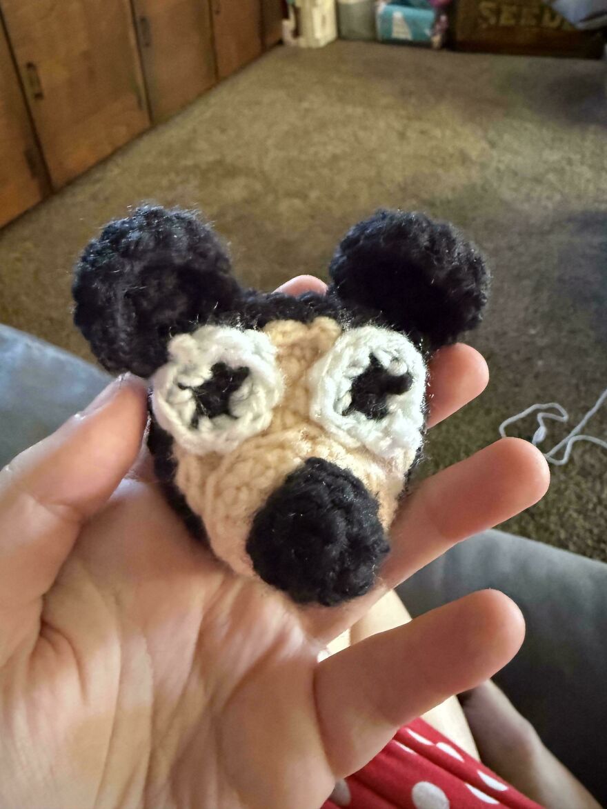 A hand holding a small, black and tan crochet creation resembling a cartoon character head.