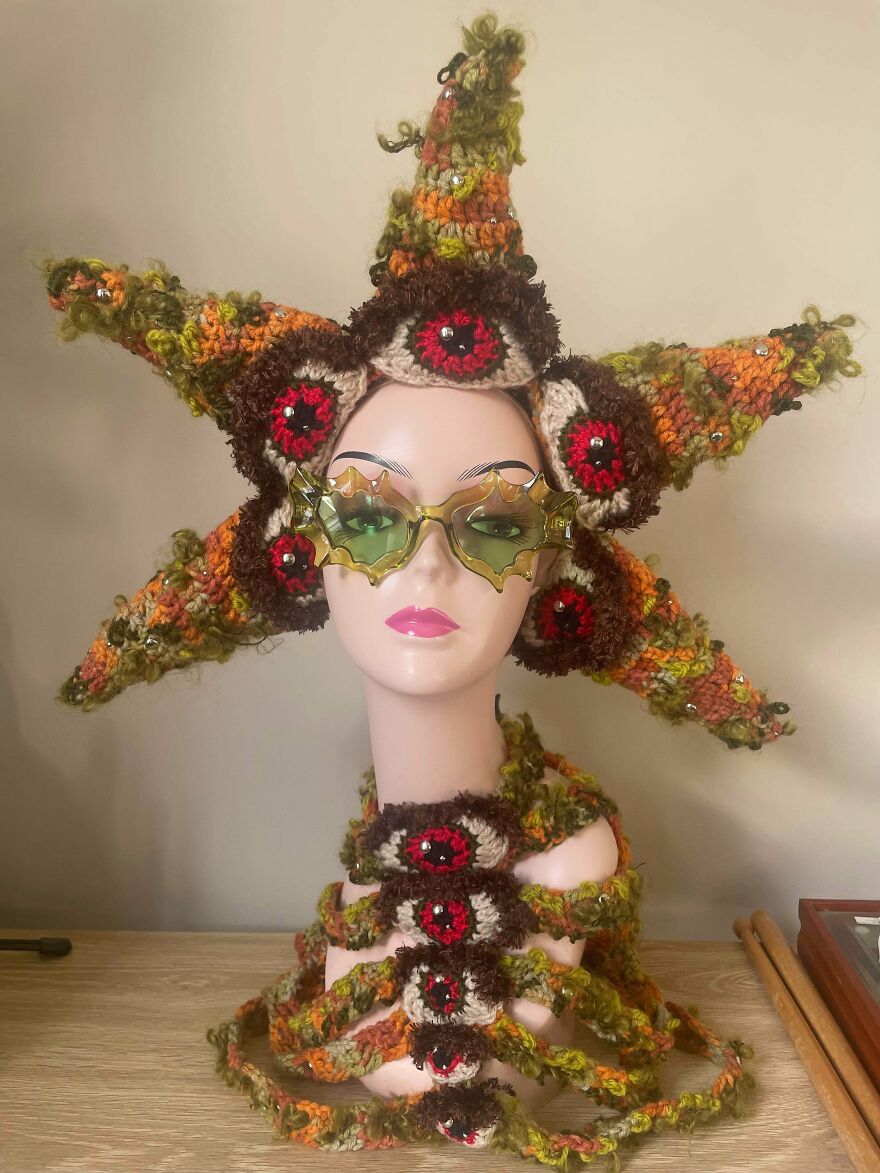 A mannequin head wearing a whimsical, multi-eyed crochet creation with a matching neckpiece.