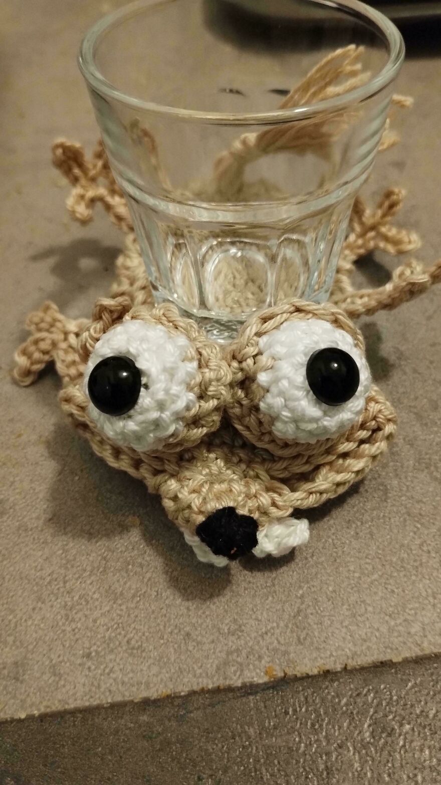 A brown crochet creation with wide white and black eyes, holding a glass, representing a unique craft project.