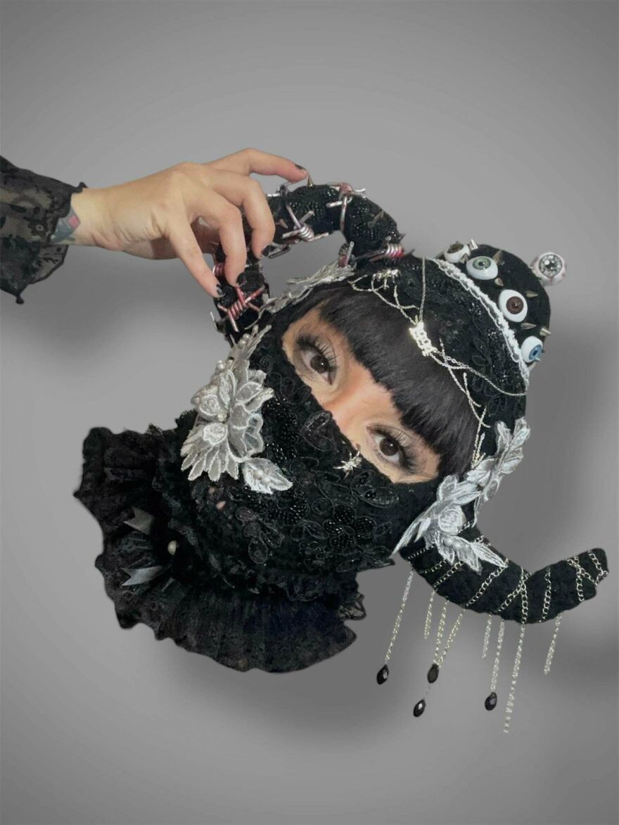 A hand holding a black lace and beaded crochet creation that covers a face, with chains and eyes, a gothic craft project.