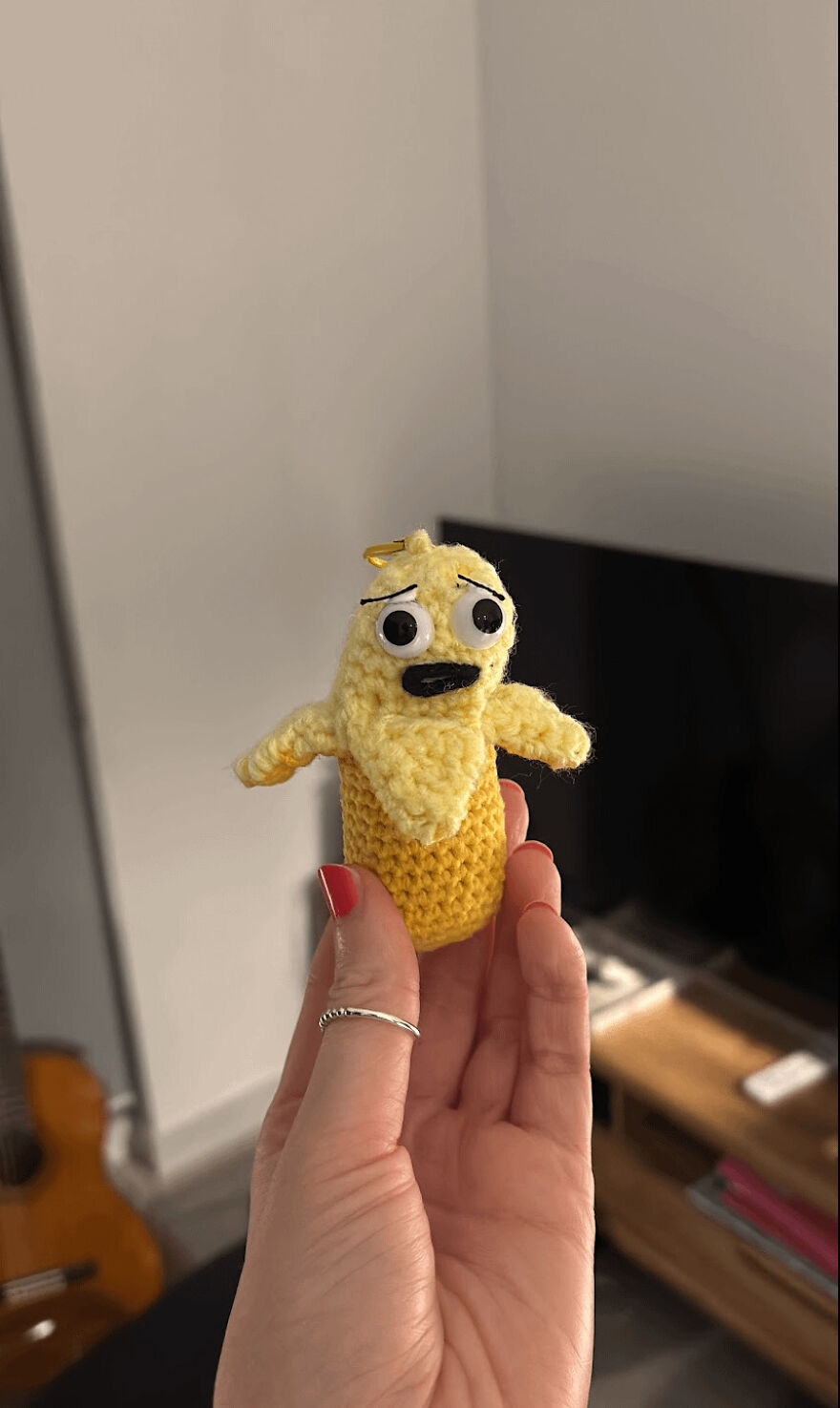 A hand holds a sad-looking yellow crochet creation of a banana character, an intended craft project.