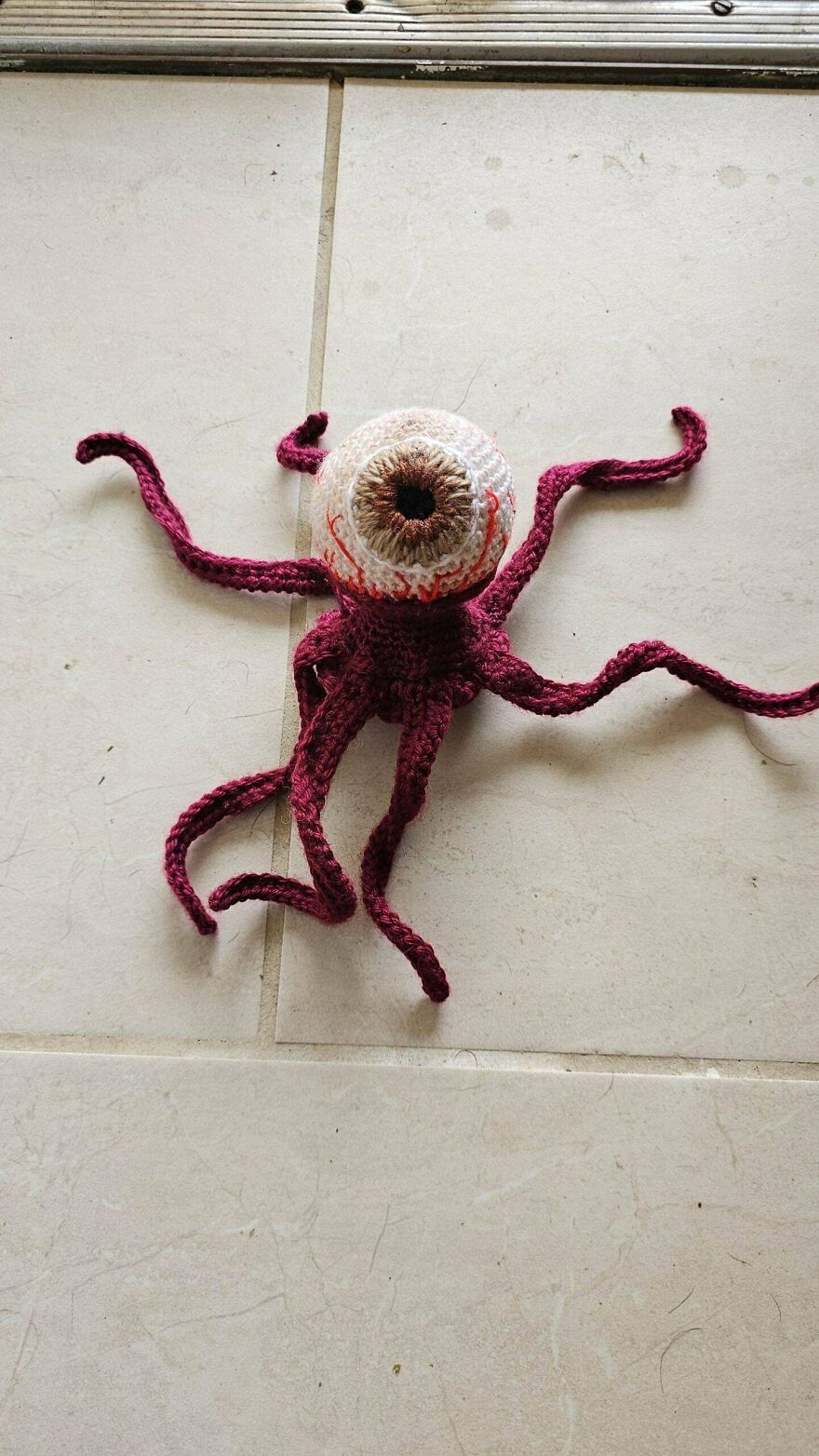 A strange crochet creation with a large eyeball and many red tentacles, an unexpected craft project.