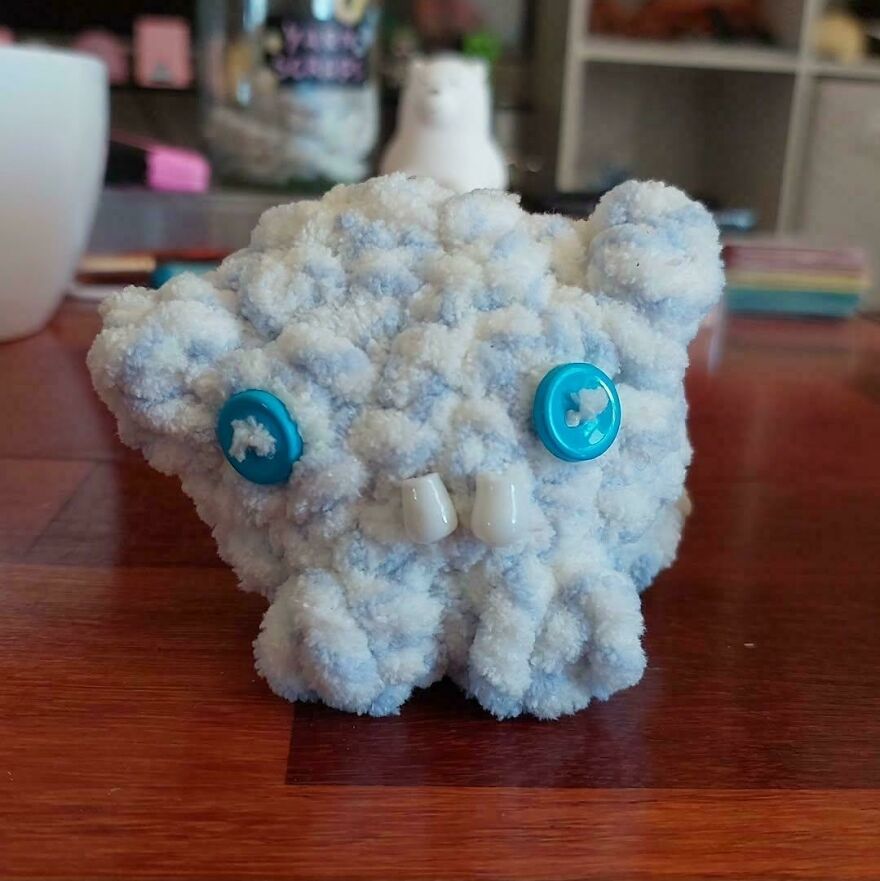 A fluffy white and blue crochet creation with blue buttons for eyes and two teeth, an unusual craft project.