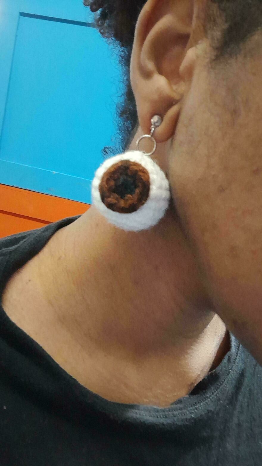 A person wearing a large, round, crocheted eyeball earring, a unique craft project that is unusual.