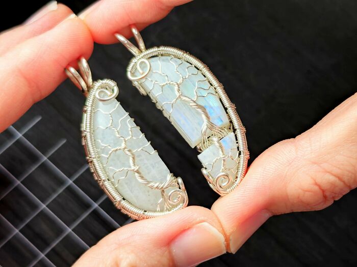 Two hands holding matching moonstone pendants with intricate wire-wrapped trees, forming a heart, a wholesome image.