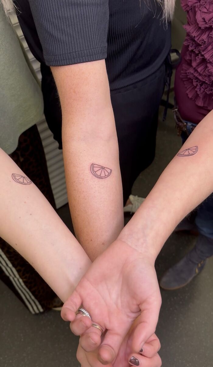 Three forearms crossed, each displaying a small, simple matching ink idea of a citrus slice tattoo.