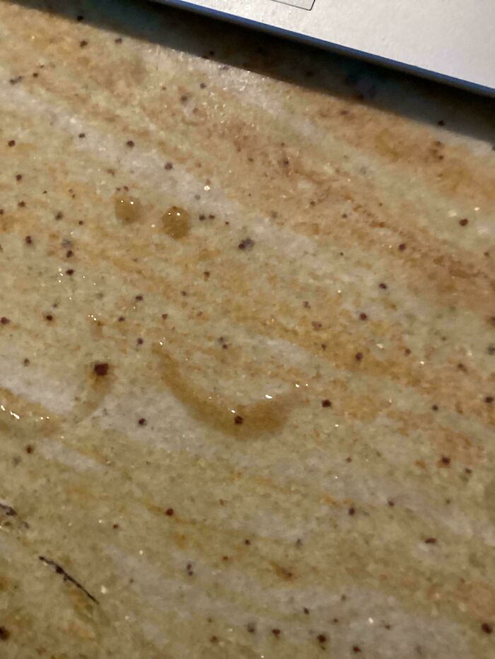Wholesome images showing water droplets forming a smiley face on a speckled countertop.