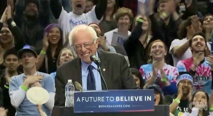 Wholesome images of Bernie Sanders smiling at a podium, with a bird perched on it, surrounded by cheering crowd.