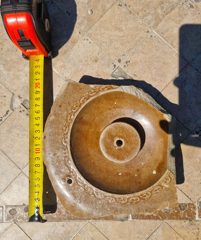 A baffling image of an old, circular stone with carved designs and a measuring tape beside it.