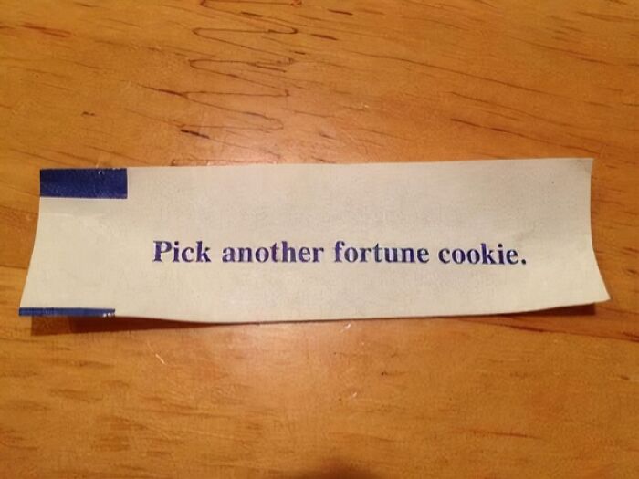 A baffling image of a fortune cookie slip on a wooden table, reading Pick another fortune cookie.