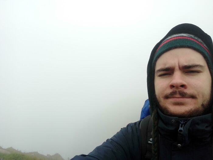 A man in a beanie and jacket takes a selfie in dense fog, showing a disappointing trip view that didn't go as planned.