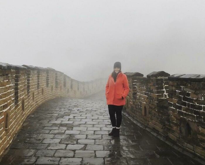A woman in a bright orange jacket standing on the foggy Great Wall of China, experiencing a trip that didn't go as planned.