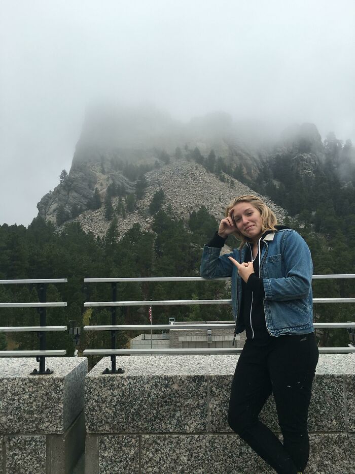 A young woman points at a mountain shrouded in fog, exemplifying a trip that didn't go as planned.