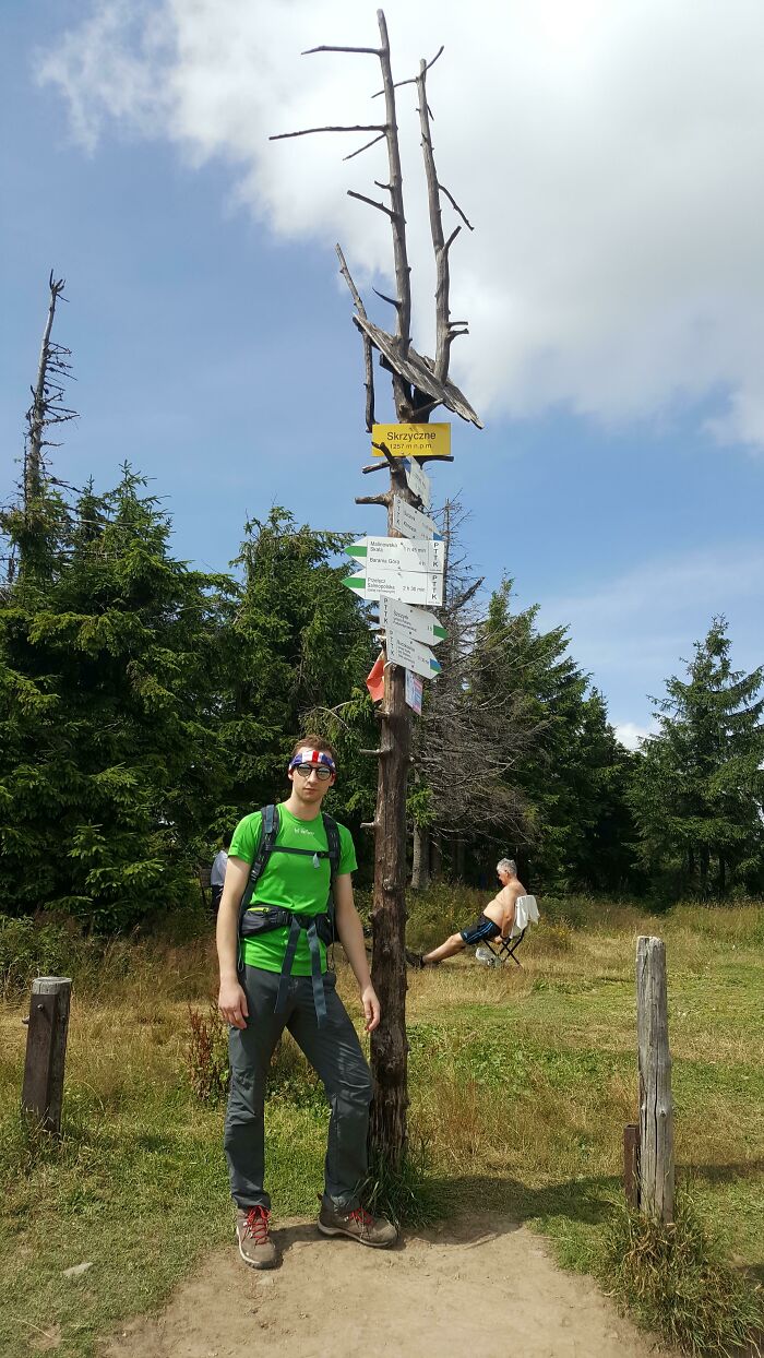 A man standing next to a wooden signpost on a hike, the trips didn't go as planned
