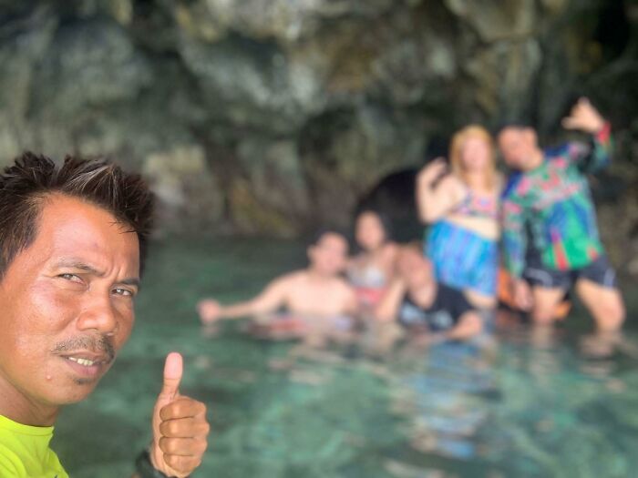 A man giving a thumbs up in the foreground while a group of people swim in a clear cave pool, an unexpected trip turn.