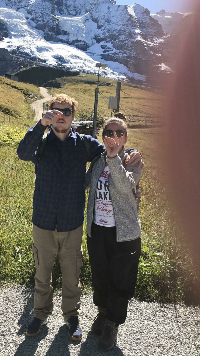 Two people standing in a sunny mountain landscape, with a bright lens flare obscuring the view, representing trips with unexpected moments.