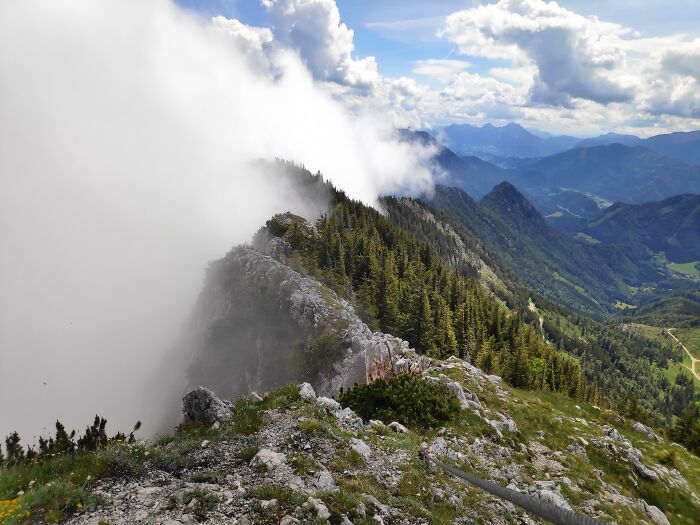 A stunning mountain ridge covered in evergreen trees and partially shrouded in clouds, exemplifying unexpected trip conditions.