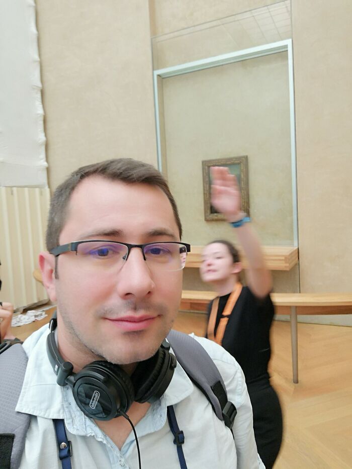 A tourist takes a selfie with a blurred Mona Lisa painting in the background, showing a trip didn't go as planned.