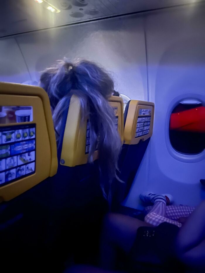 Long blonde hair draped over the back of an airplane seat, impacting other people's trips.