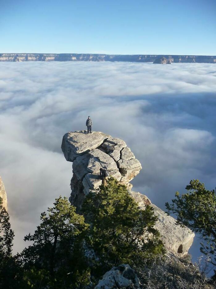A person stands on a rock formation above a sea of clouds, a scenic trip despite obscured views.
