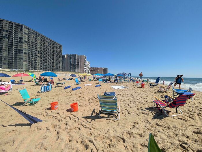 A crowded beach scene showing many entitled folks with beach chairs and umbrellas on a sunny day.