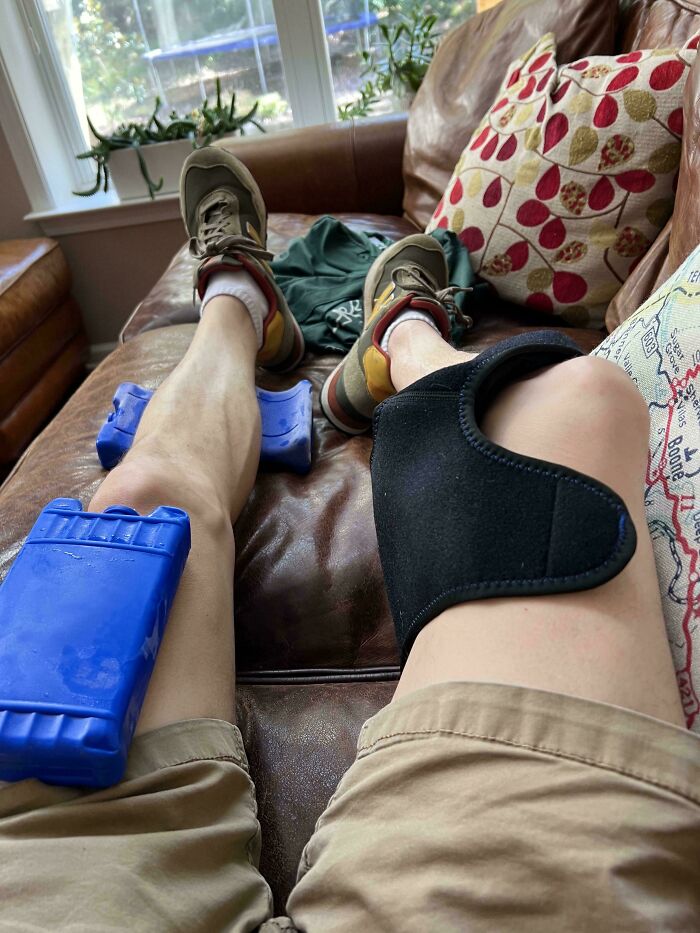 Legs with ice packs and a knee brace on a couch, showing a trip injury or unexpected event.