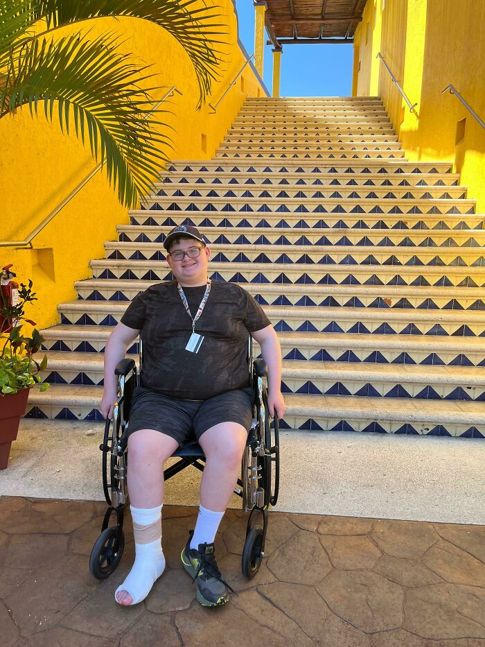 A man in a wheelchair with a bandaged foot at the base of long, colorful stairs, highlighting a trip mishap.