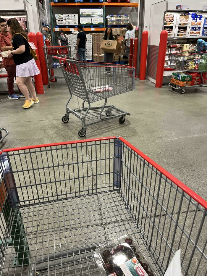 A shopping cart left in a busy Costco aisle, showing entitled folks ignoring others in their world.