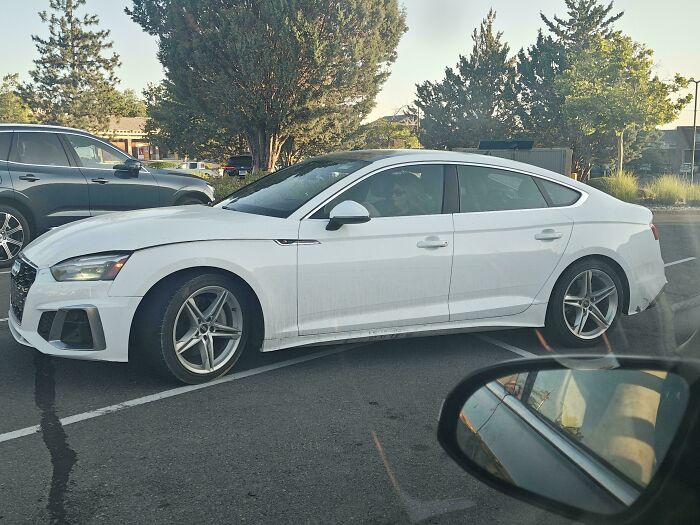 An entitled driver has poorly parked a white Audi across two parking spots, taking up extra space.
